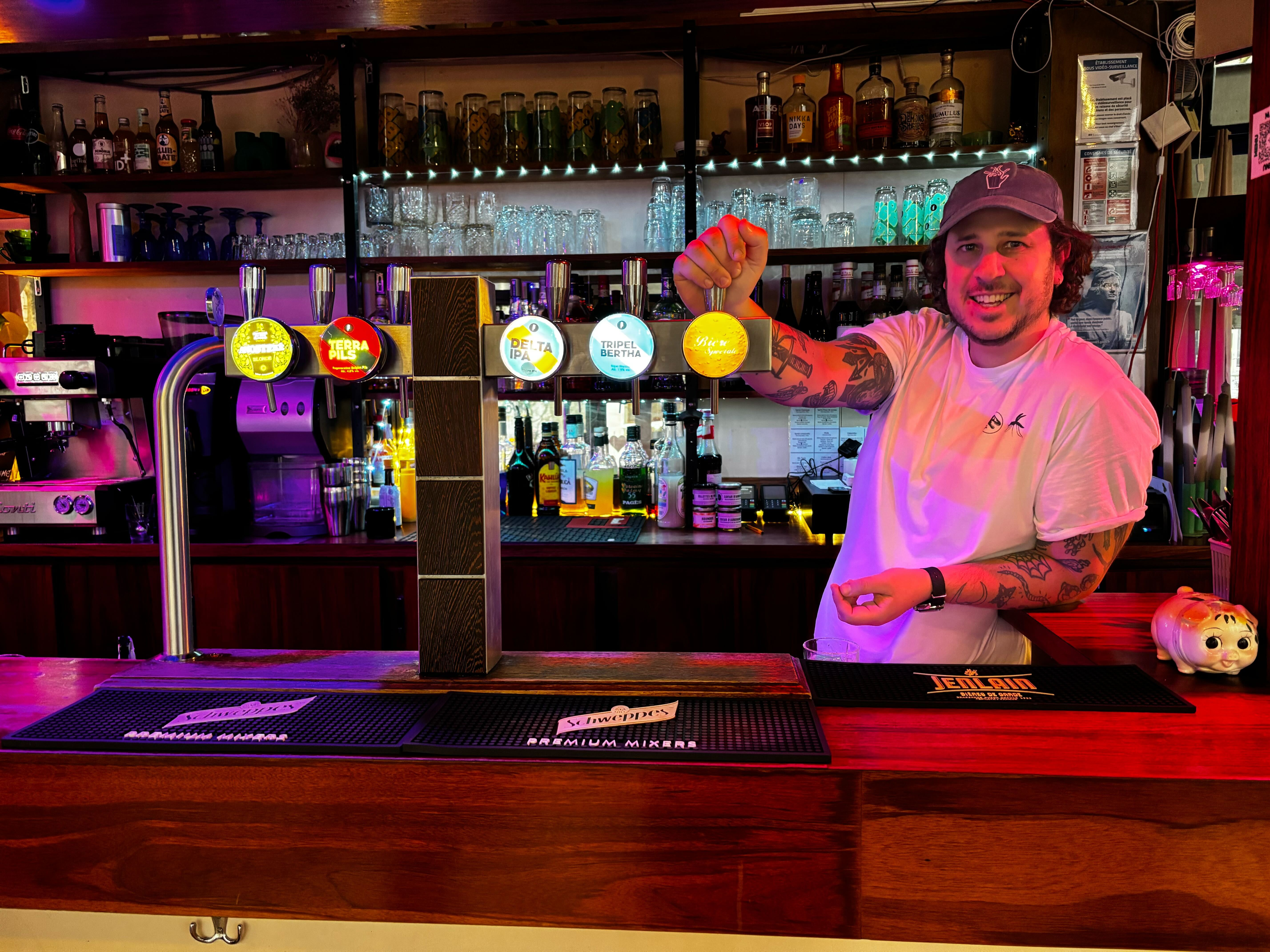 Un homme derrière un bar avec un tee-shirt blanc et une casquette
