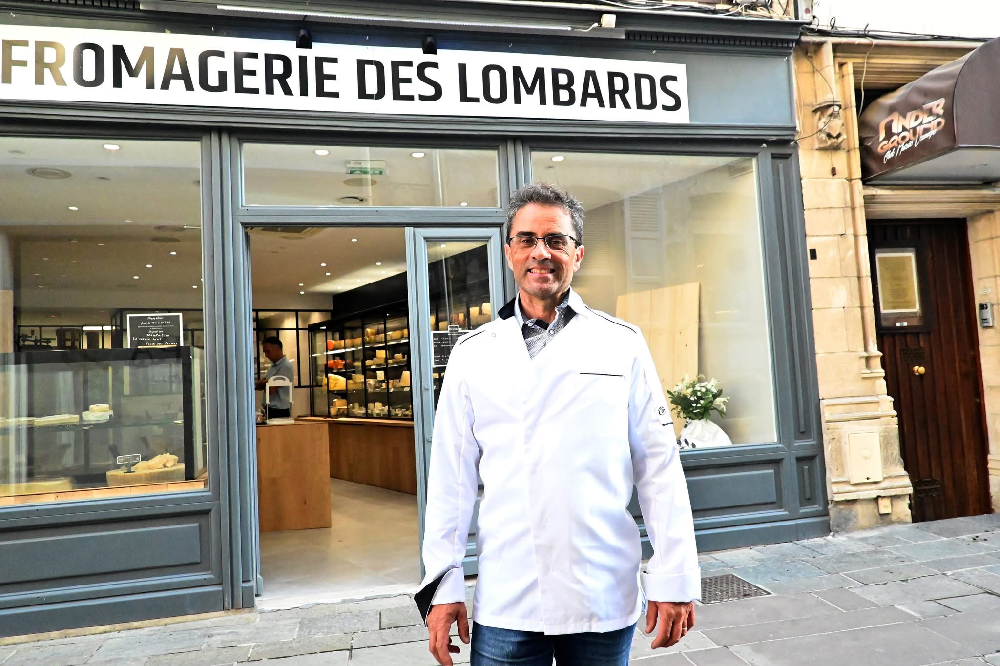 Homme en blouse blanche devant une fromagerie