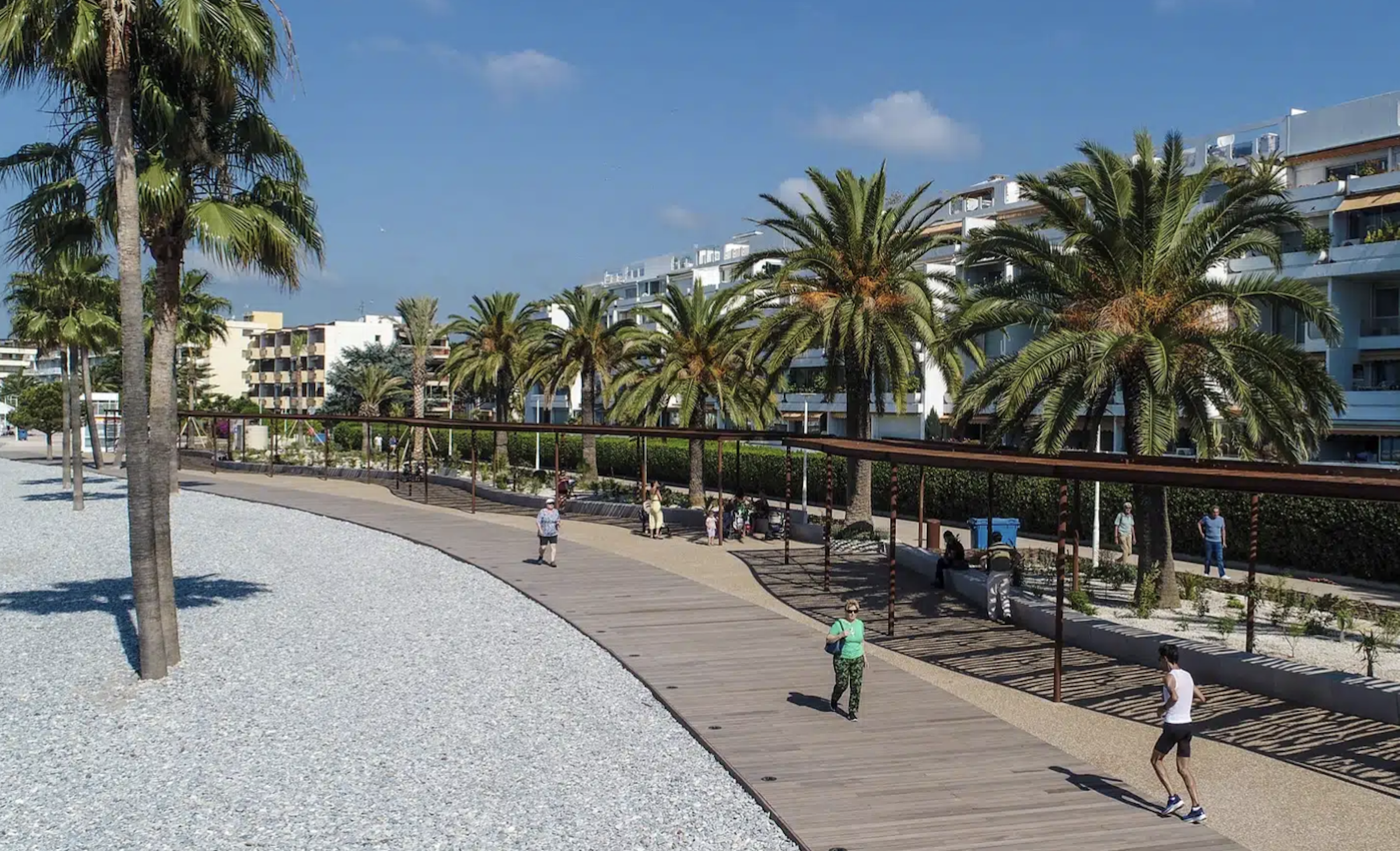 Vue sur Saint-Laurent-du-Var avec sa plage, ses palmiers et un chemin oĂč des personnes se baladent.