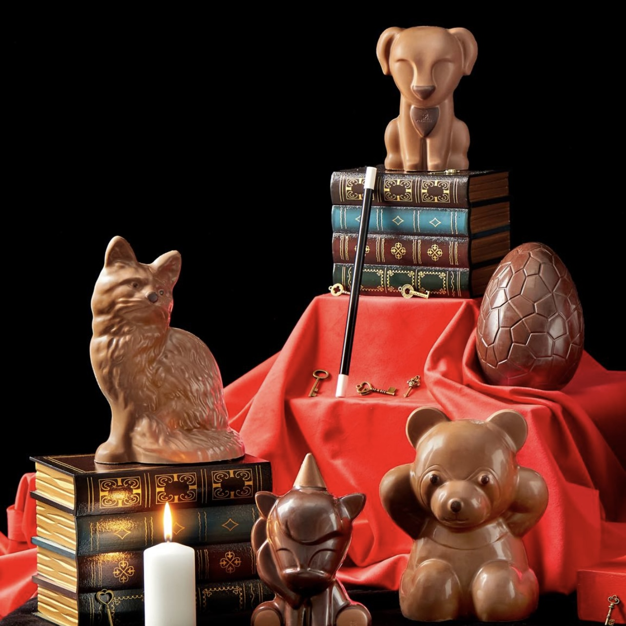Plusieurs figurines en chcolats disposé ans un décor rouge avec bougie et livres