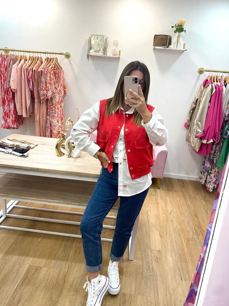 Femme dans un miroir portant un jean, une chemise blanche, un gilet rouge