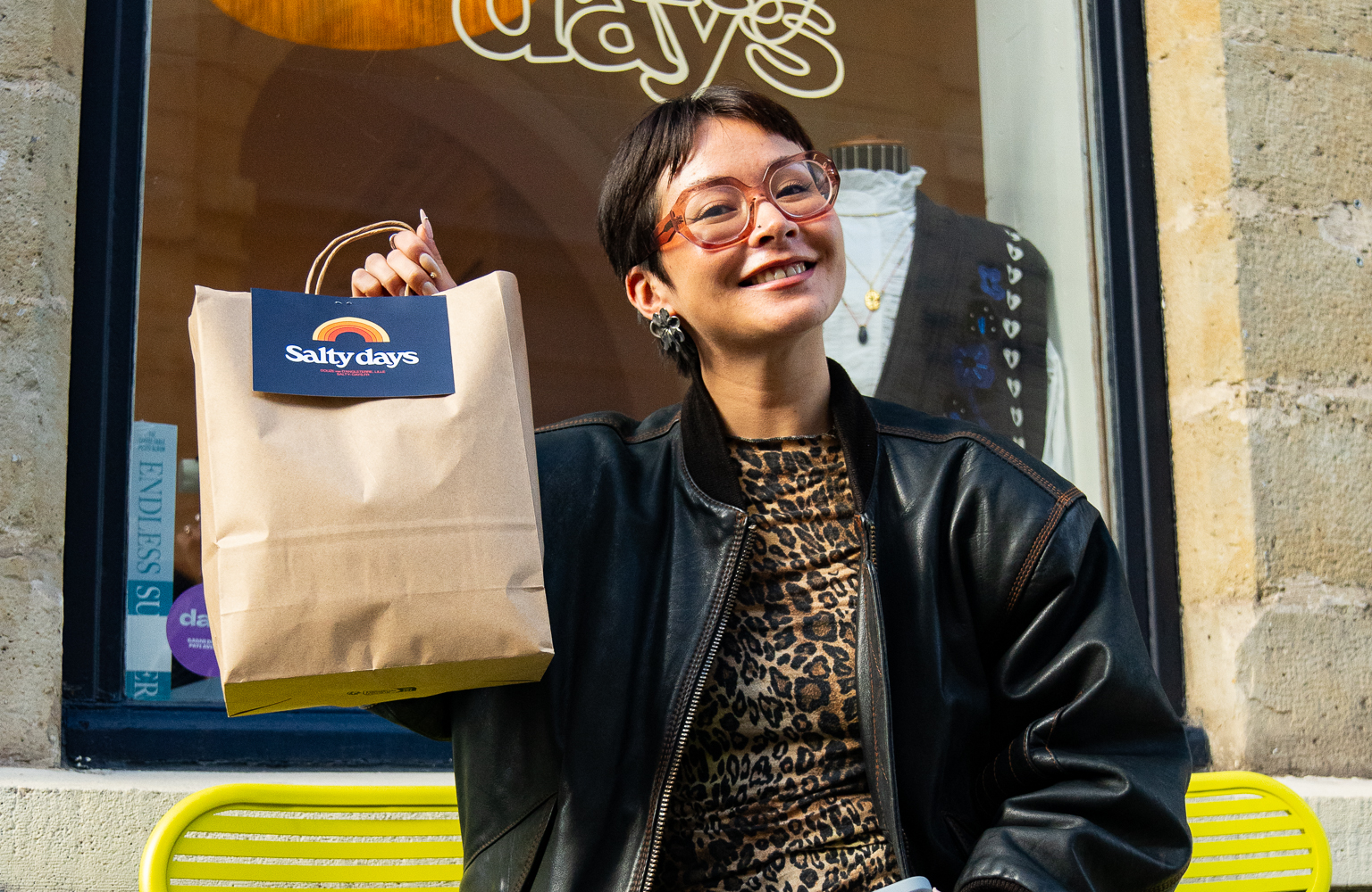 Femme souriante assise sur un banc jaune avec un sac
