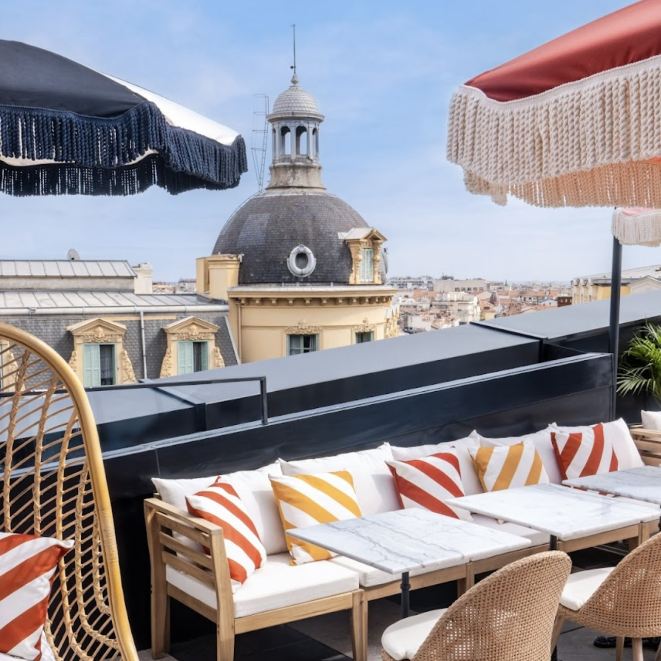 Terasse avec canapés, coussins, chaises et parasols. Vue sur les toits en fond.
