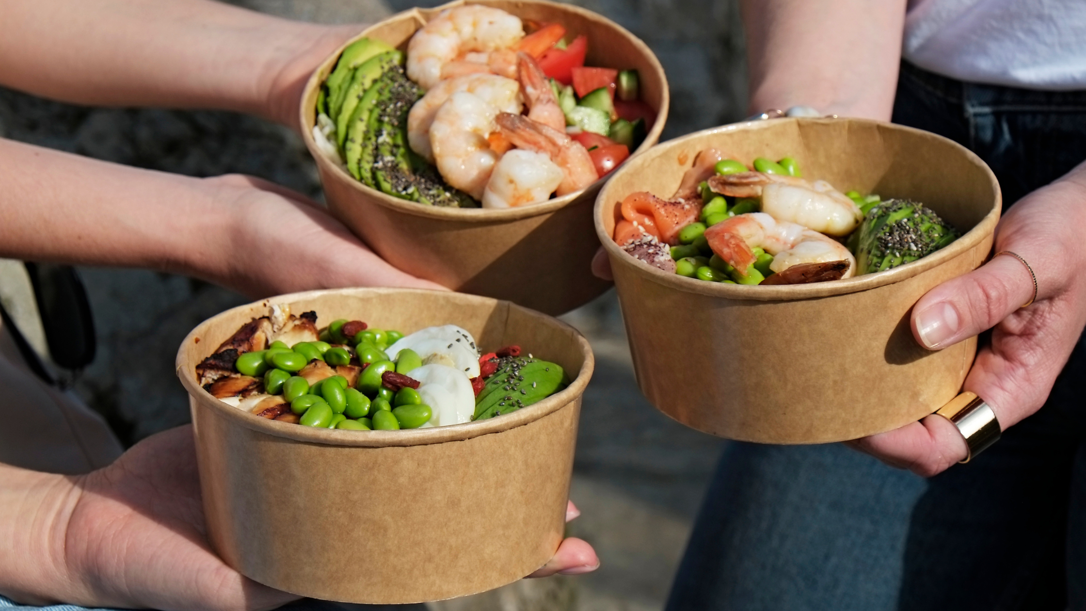 Trois poké bowls tenus par trois personnes