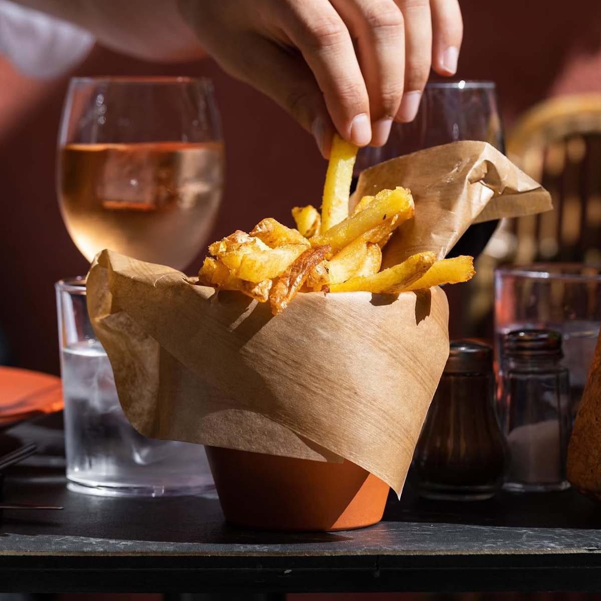 Main prenant une frite avec verre de vin dans le fond
