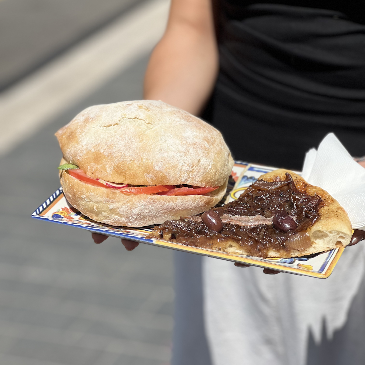 Personne tenant une assiette avec un pan bagnat et une pissaladière à l'intérieur