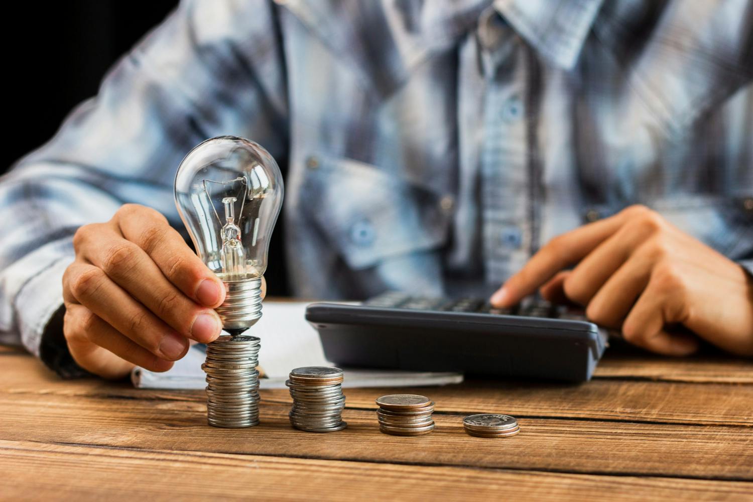 imagem ilustrativa de um homem segurando uma lâmpada sobre moedas e, ao lado, uma calculadora.