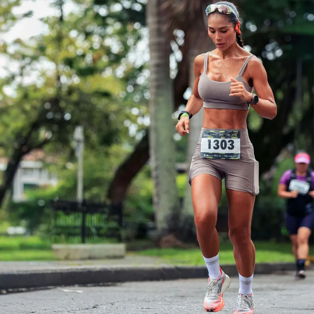 Mulher correndo ao ar livre em parque verde, usando roupas de corrida, traje esportivo e número na camiseta, praticando exercícios ao ar livre.