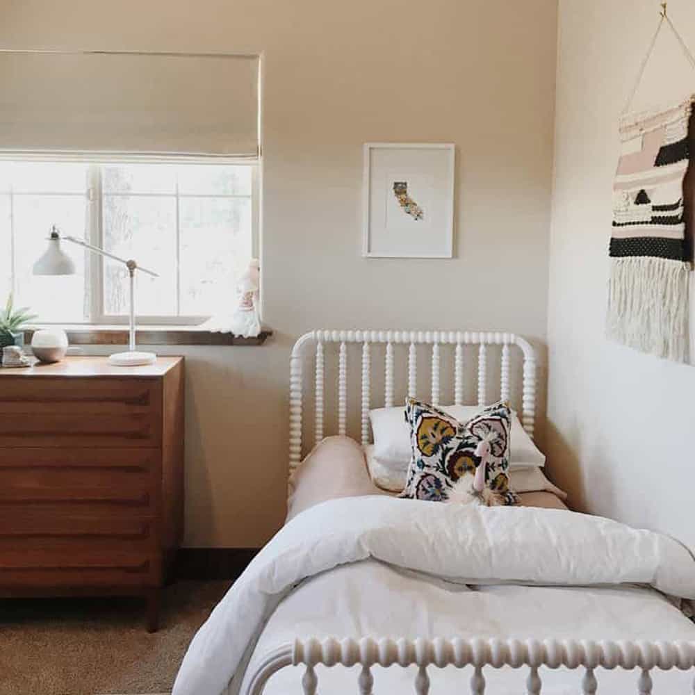 Girl's room with neutral pink and white bedding, wall tapestry, and off white roman shades in the window.