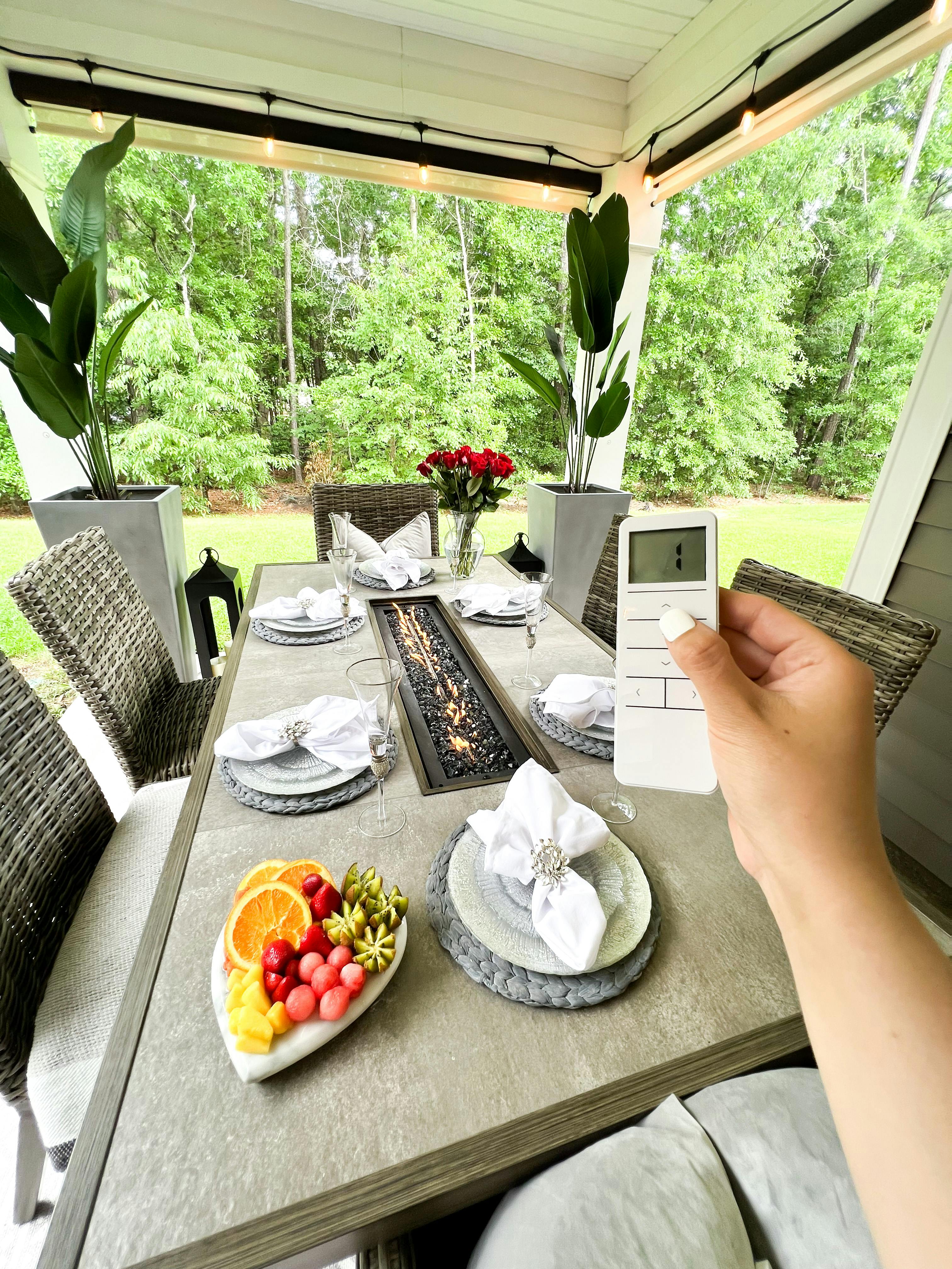 A remote operating Blinds.com Heavy Duty Outdoor Shades in an outdoor dining area