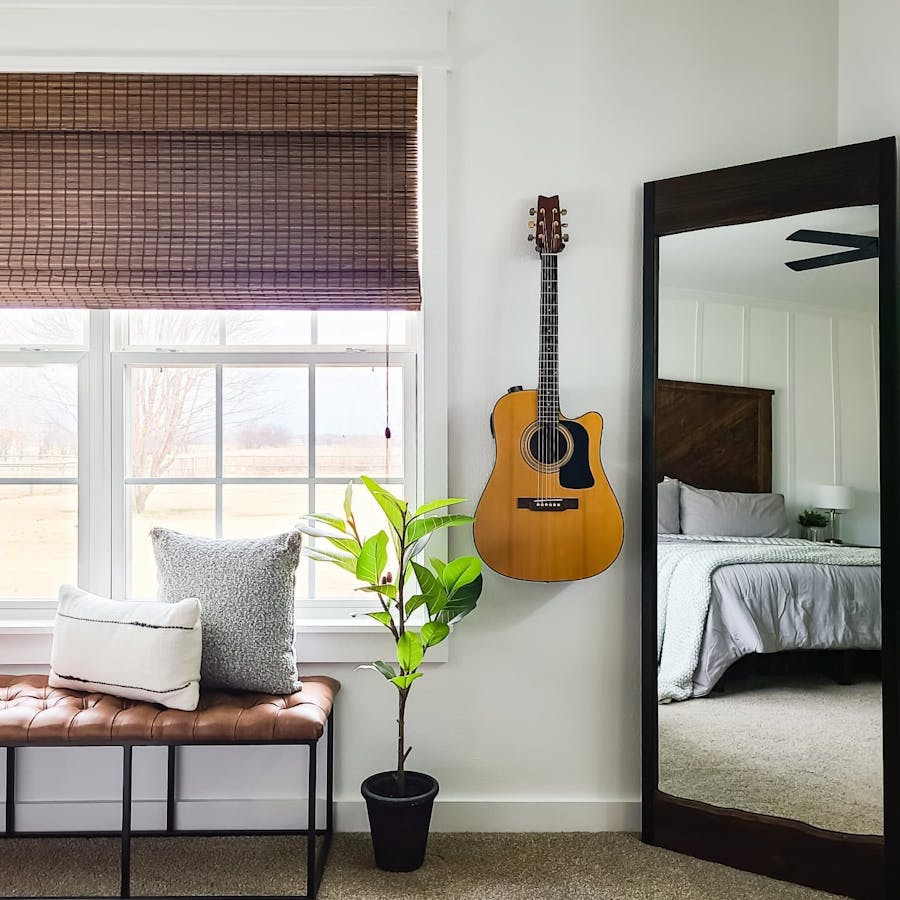 a bedroom with a guitar on the wall and woven wood shade window treatments