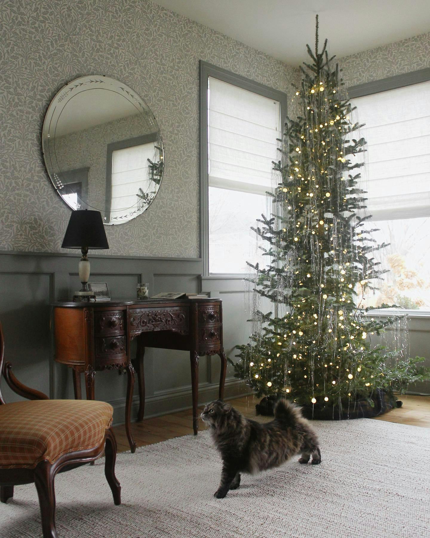 christmas tree covered with tinsel in front of corner window with roman shades 