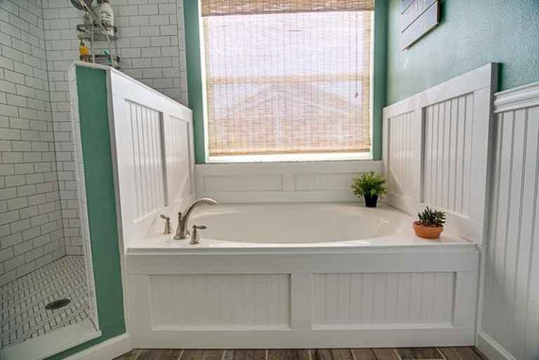 green and white bathroom with subway tile, beadboard walls and bamboo shade over bathtub