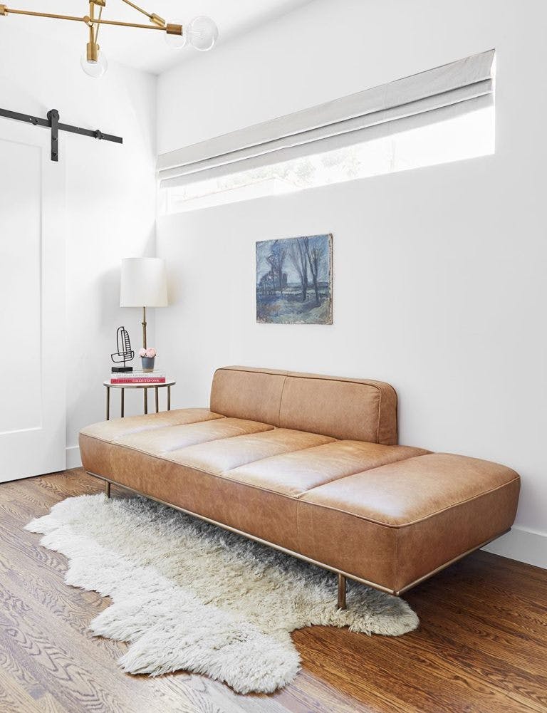 corner of living room with leather bench under long skinny window with grey roman shade