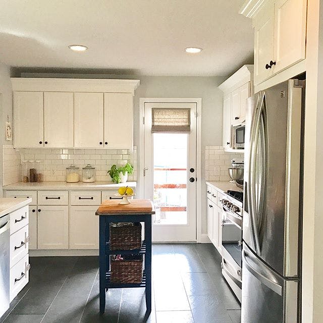 white kitchen with movable island and back door with tan linen roman shades