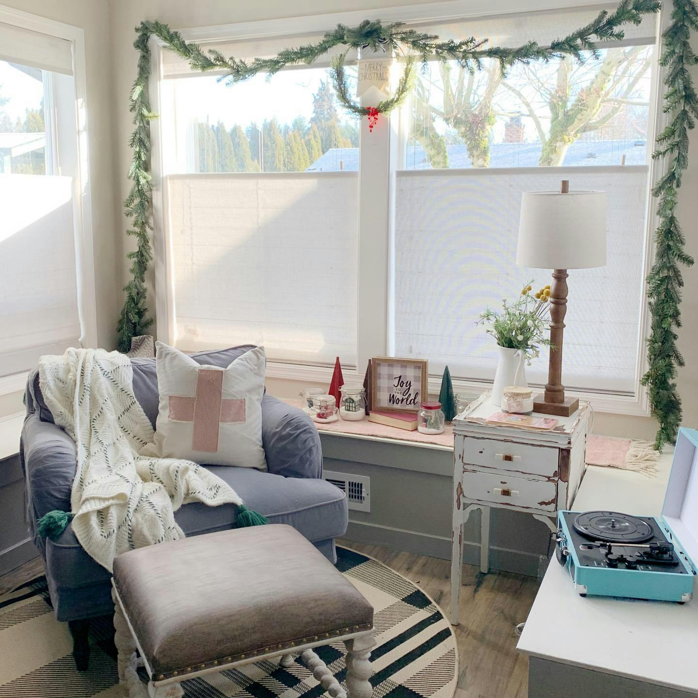 Living room holiday display that includes garland and small wreath with red accent underneath.