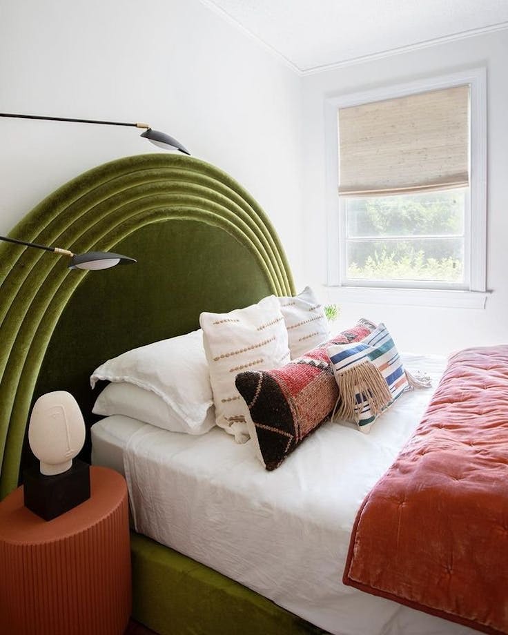 Bedroom with green headboard and pink blanket. Woven wood shades are on the window.