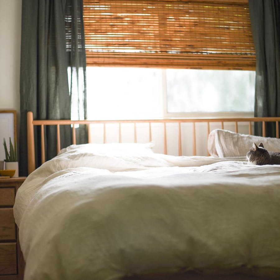 a dimly lit bedroom with natural sunlight peeking through. cordless woven wood shades are on the window over the bed.
