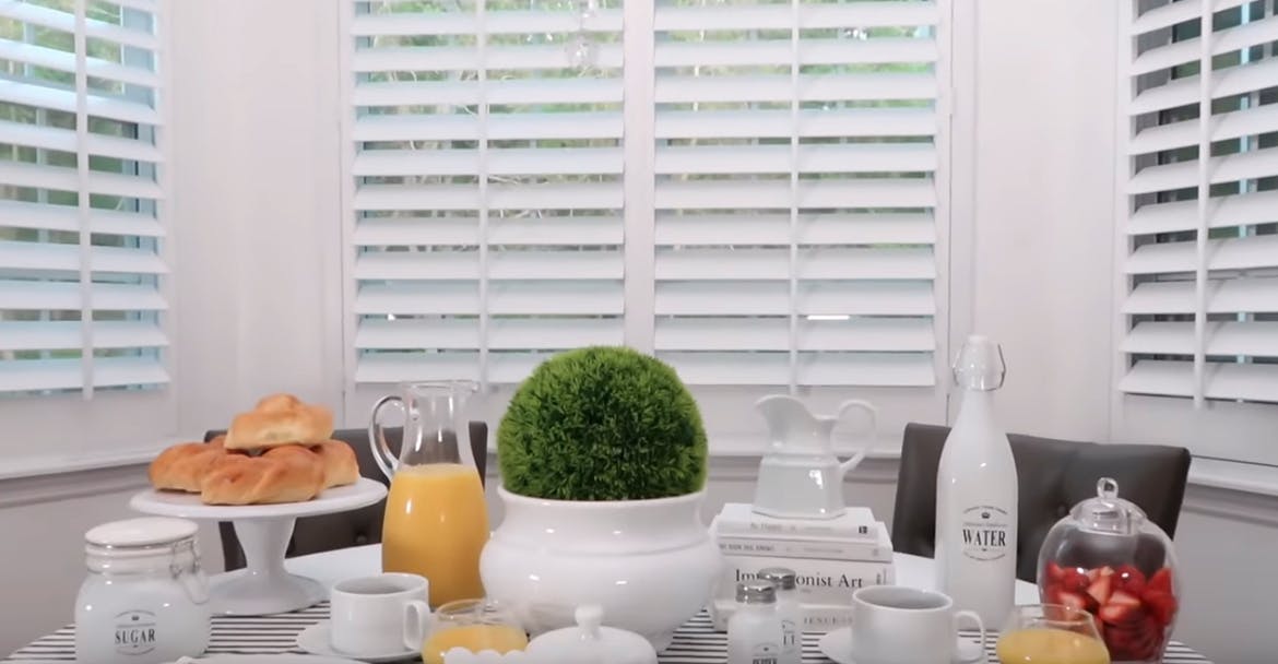 breakfast table set with brunch in front of bay window shutters