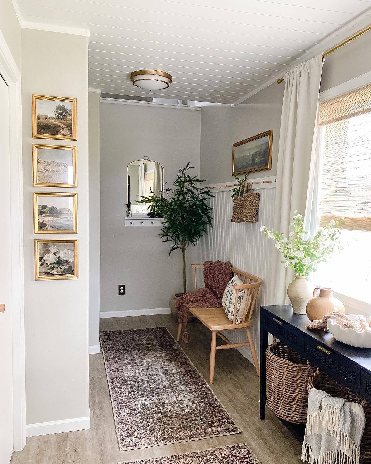 An entryway decorated for fall with a paisley runner and small table with baskets stored underneath. There are beige woven wood shades from Blinds.com on the window.