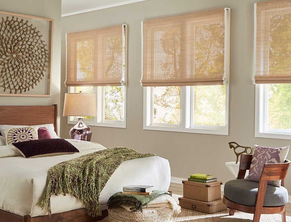 Bedroom with three large windows covered by woven wood shades.