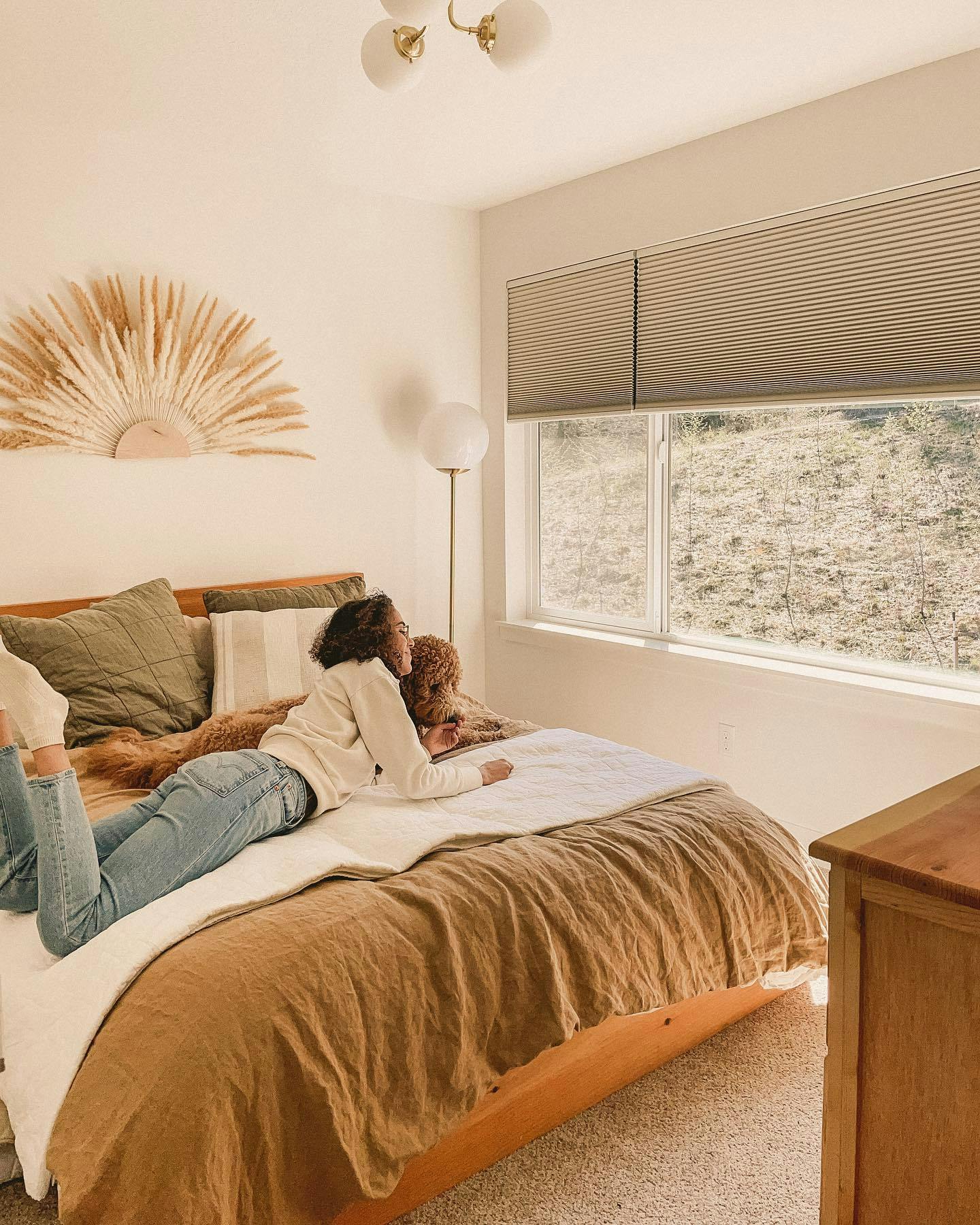 woman lays on bed with dog looking out window with blackout window shades