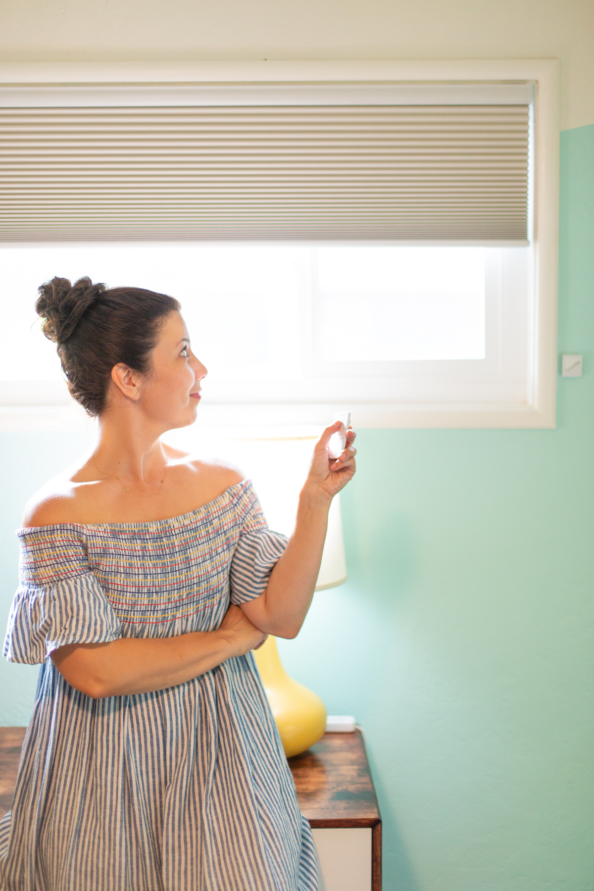 A woman pointing a remote toward her Blinds.com motorized shades