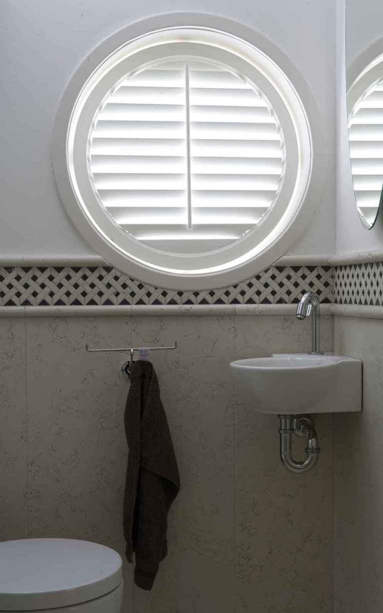 circle window in bathroom covered with custom plantation shutters
