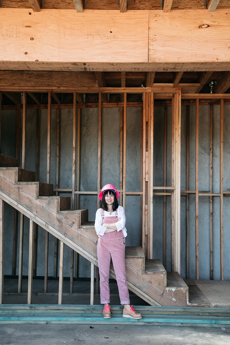 Joy cho wearing pink overalls standing in front of stairs on construction site