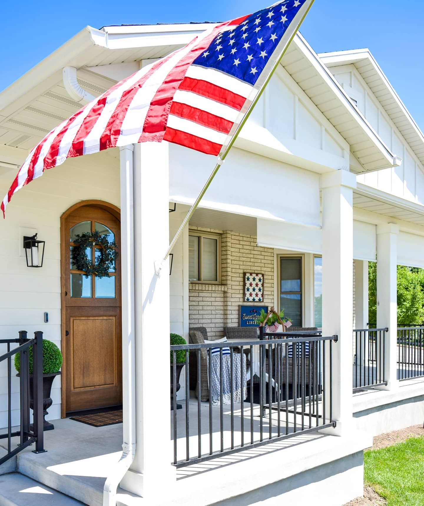 white house with with white outdoor solar shades. American flag on the front of the house flowing in the wind. 