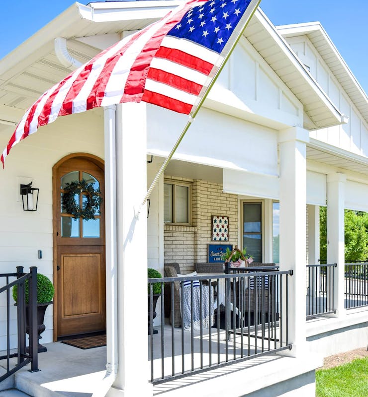 white house with with white outdoor solar shades. American flag on the front of the house flowing in the wind.