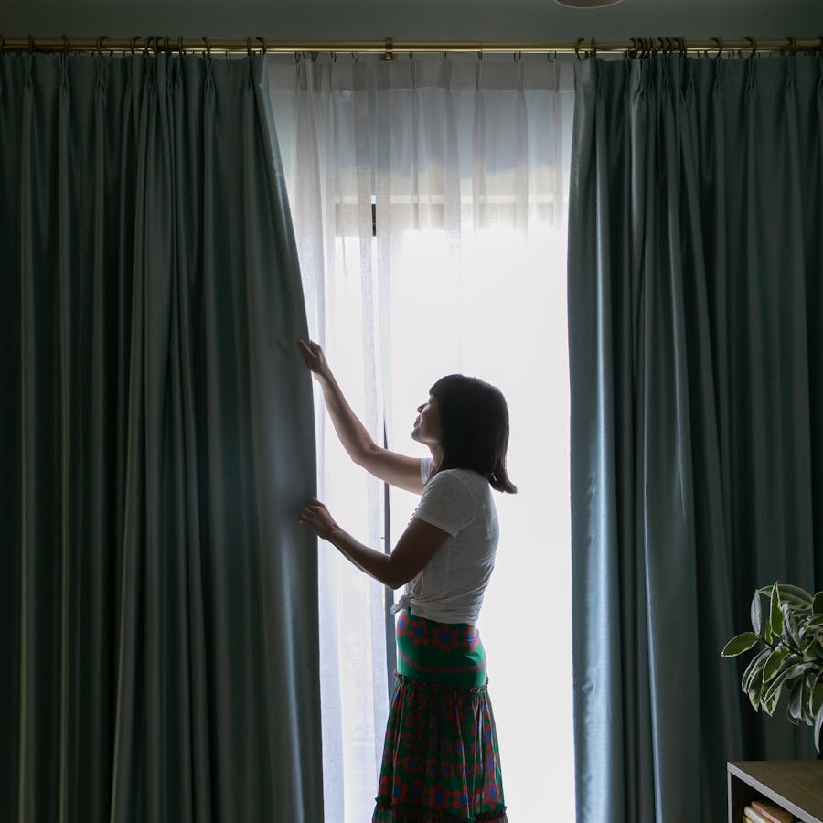 A woman closing her Easy Classic Pleat and French Pleat Drapery in her bedroom.
