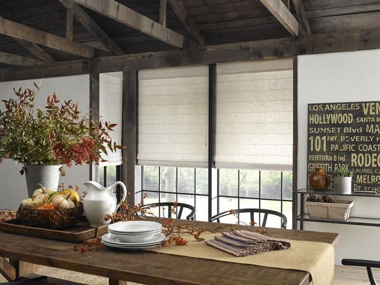 long dining table with inset bay window behind covered with white linen roman shades