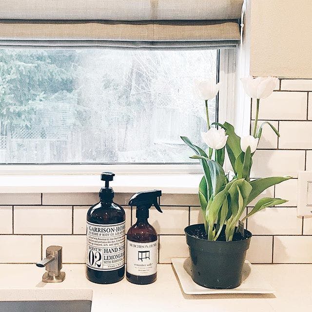 windowsill behind sink with pretty hand soap, tulips in pot and greige roman shades on window