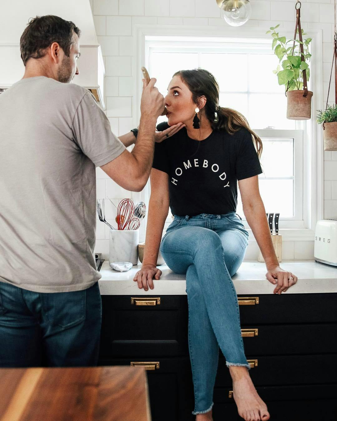 Man giving woman taste of recipe while she sits on kitchen counter