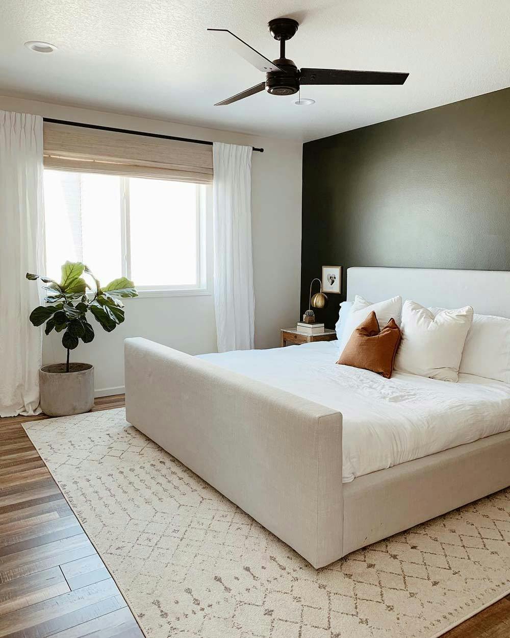 minimalist bedroom with dark green accent wall and woven window shades
