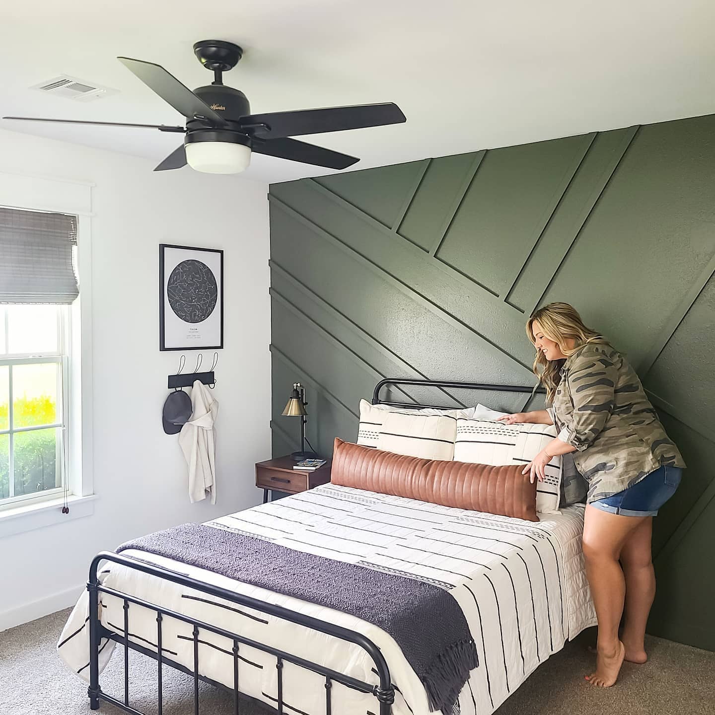 a woman is making a bed and woven wood shade window treatments are in the corner