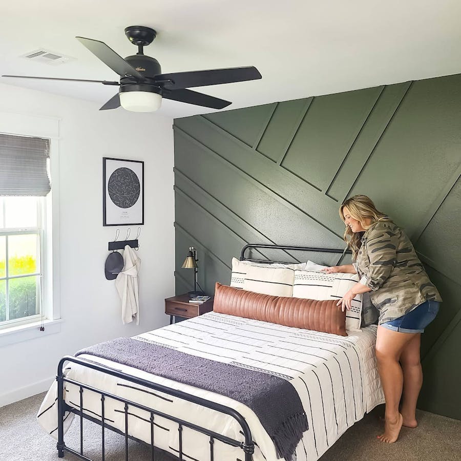 a woman is making a bed and woven wood shade window treatments are in the corner