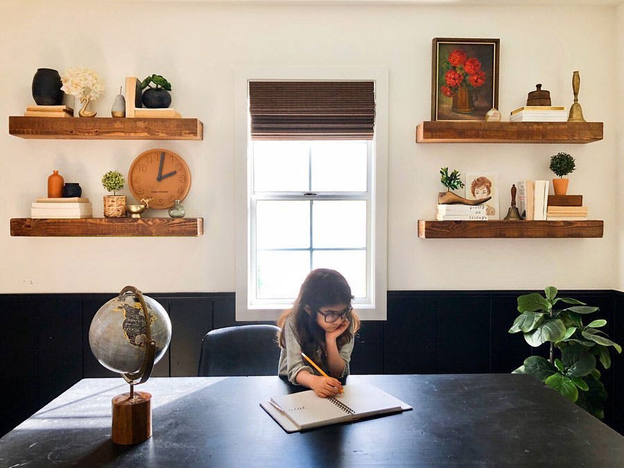 girl working at homeschool desk in office with woven wood shades and open shelving