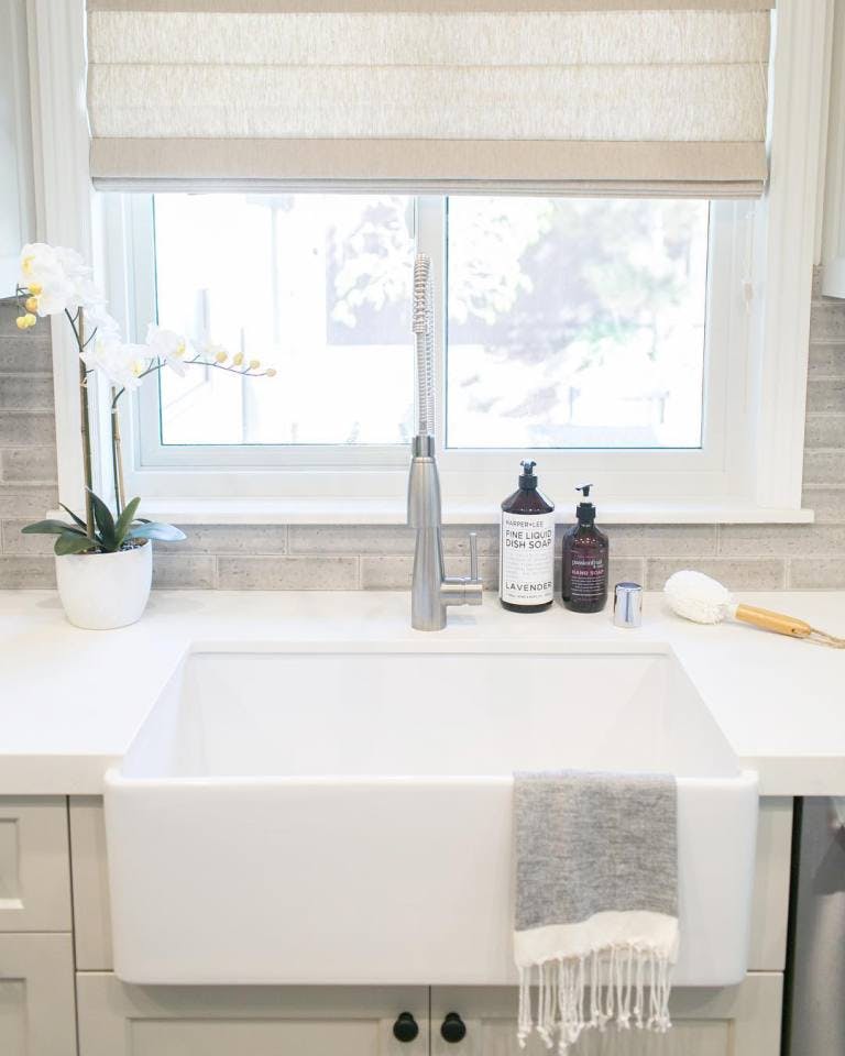 Kitchen with apron sink and light beige roman blinds over window behind sink