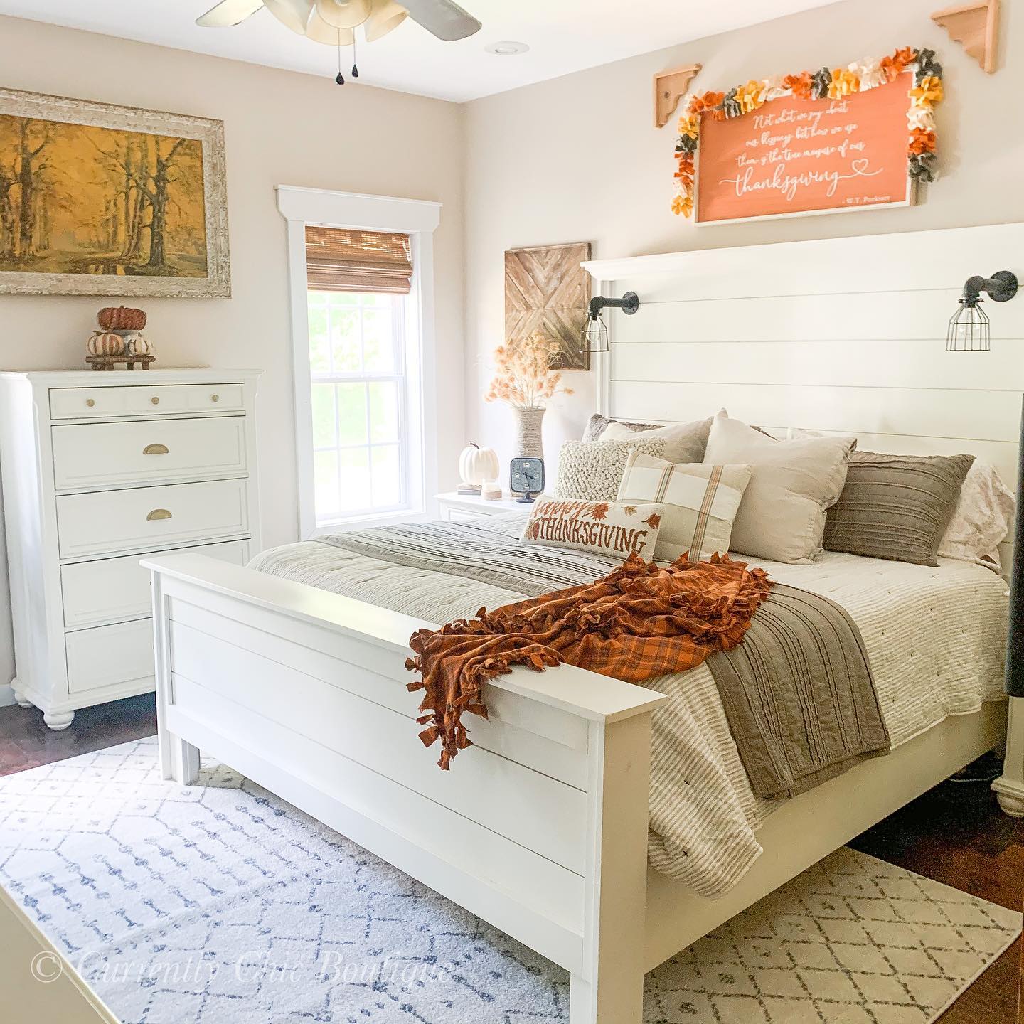 Bedroom decorated for Thanksgiving with orange blankets and neutral accent pillows. Woven wood shades are covering the window.