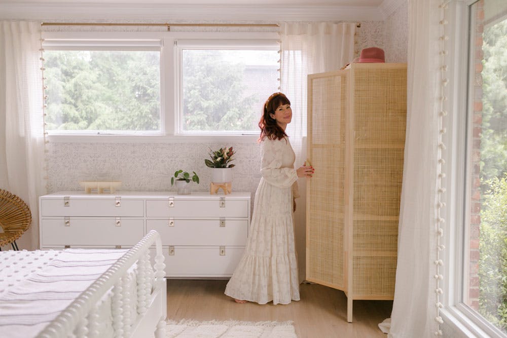 woman in white dress opens cabinet in neutral bedroom with blackout shades