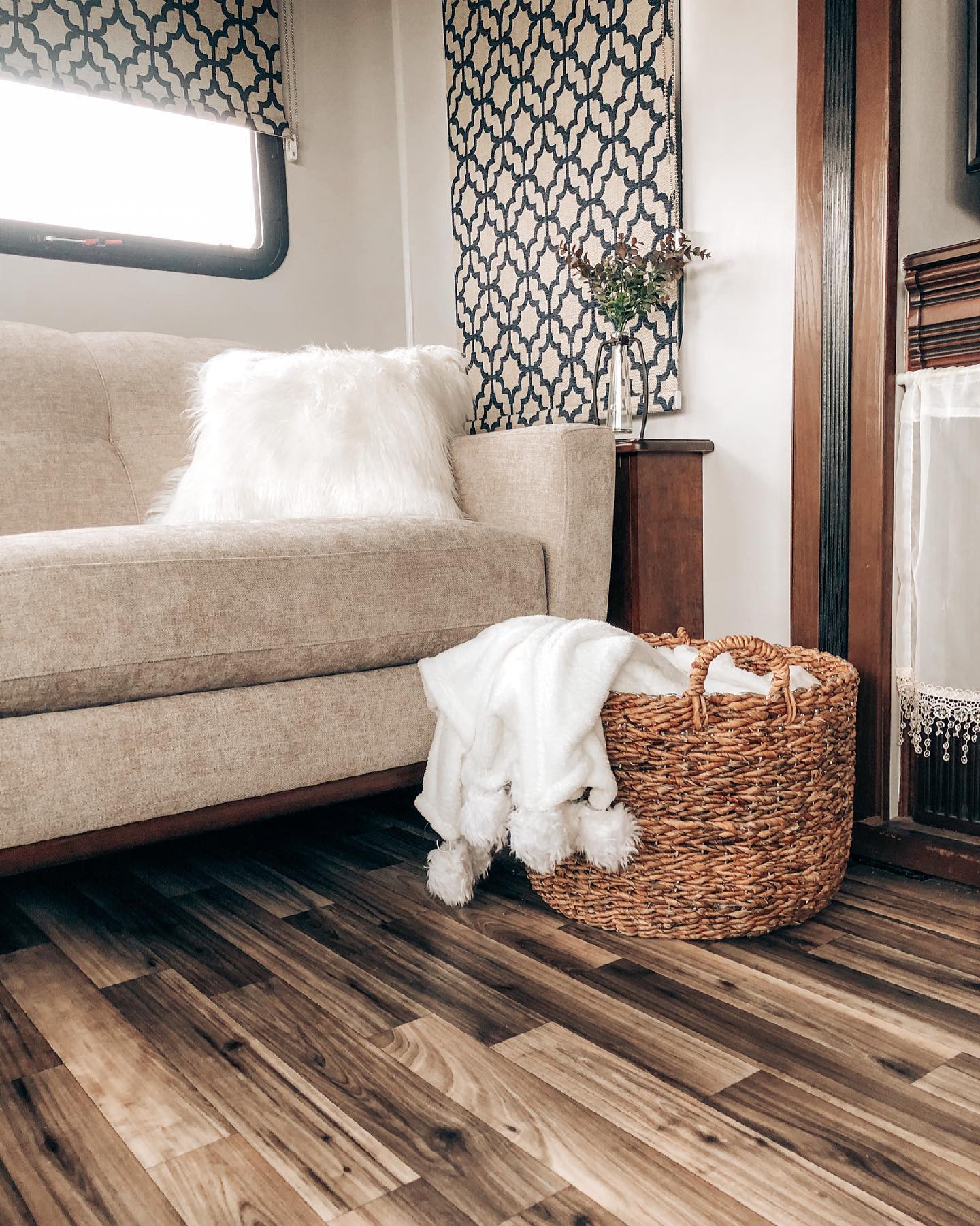 There is a gray sofa with a woven basket beside it inside of an RV. There is a cozy white blanket inside the basket.