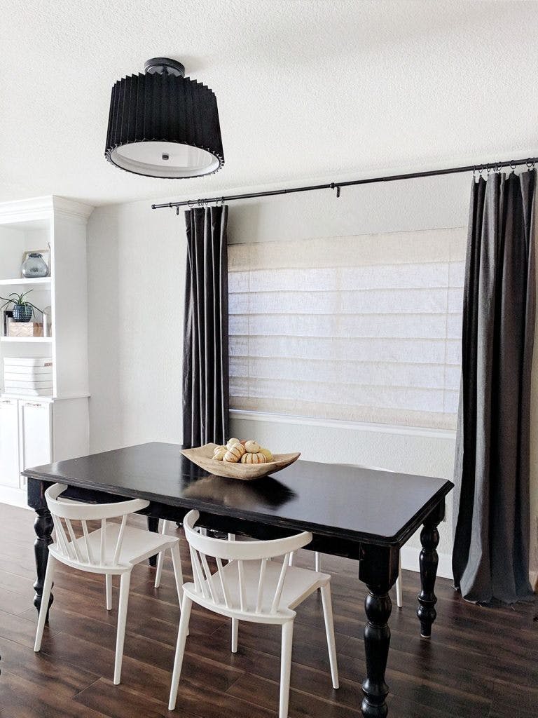 dining table in front of large window with off white roman shades and dark grey curtains