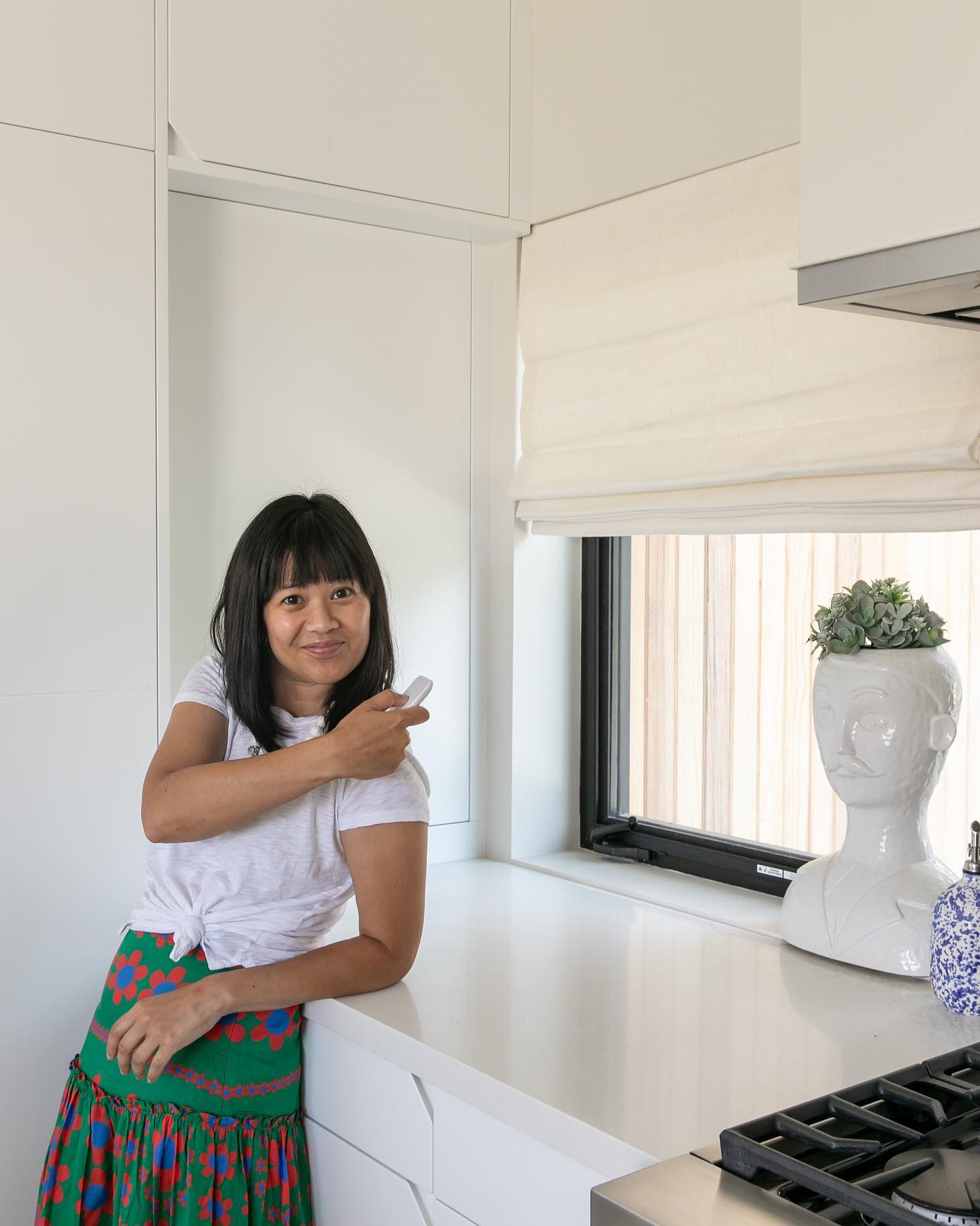 a woman its holding the remote to her motorized roman shades
