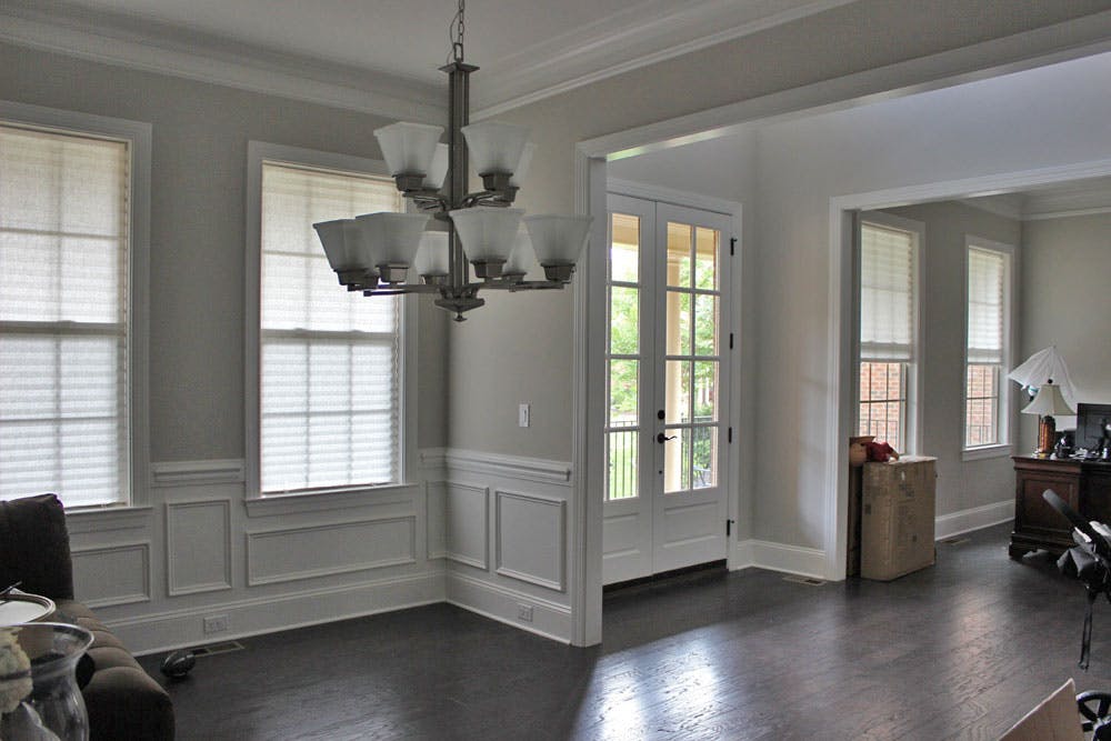 spacious, open concept living and dining room with two windows covered with cellular shades on each side of the french doors (which are not covered with shades).