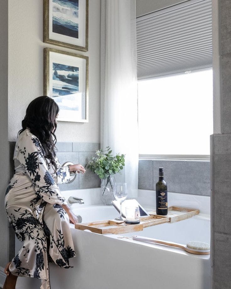 A woman sitting on the edge of a bathtun with simplyeco cellular shade window coverings on the window