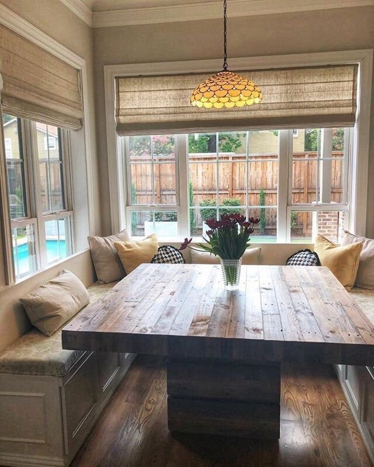 built in kitchen dining booth with bench seating and tan linen roman shades on windows.