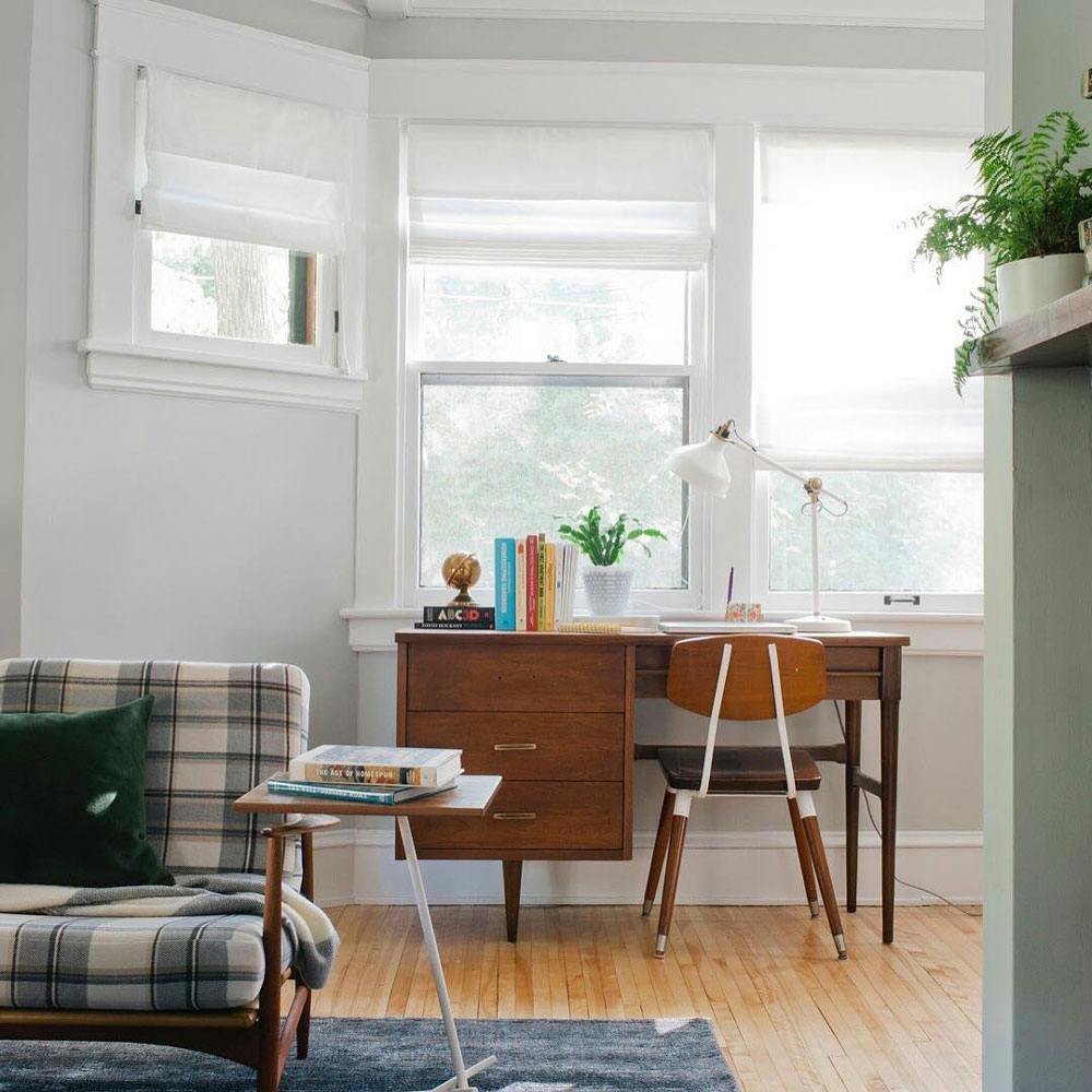 child's homeschool desk in corner of living room facing window with white roman shades