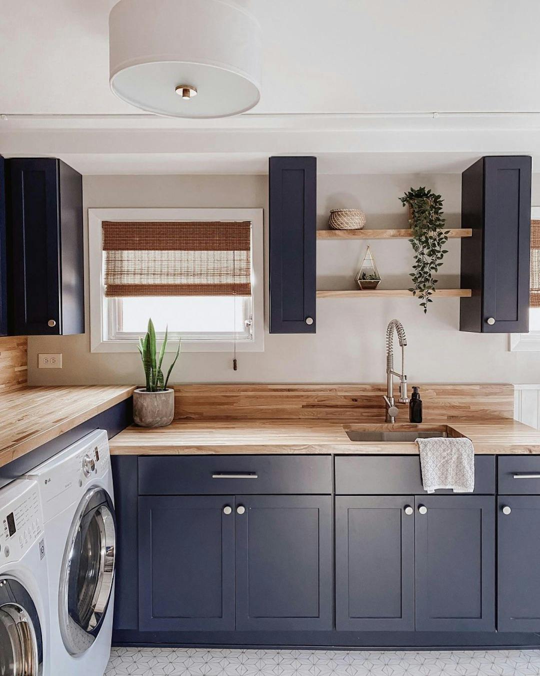 Laundry room with navy blue cabinets and a wood countertop. There is a small snake plant on the counter.